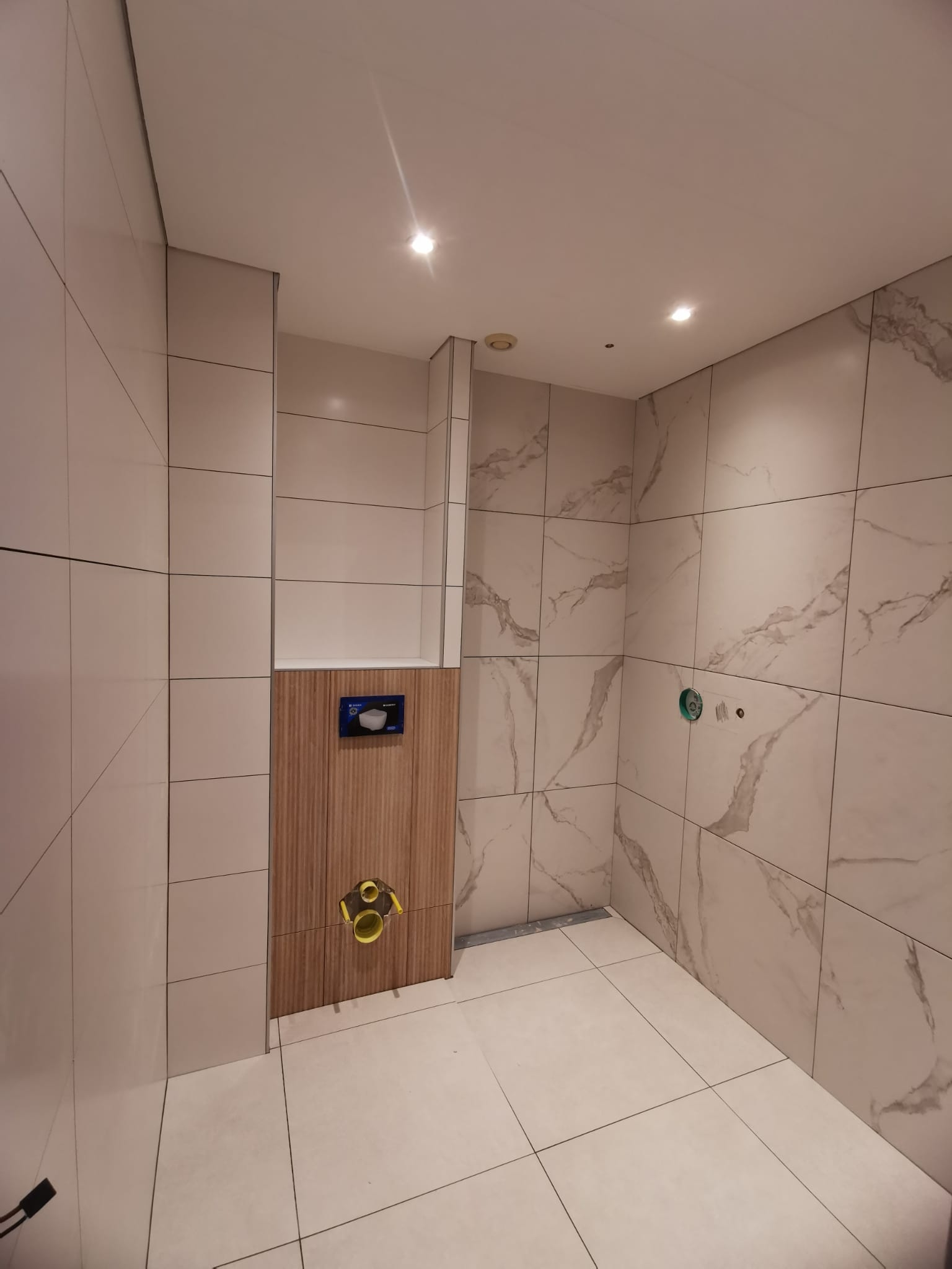 Badkamer in aanbouw met grote tegels in marmerlook en een betimmerd toiletframe